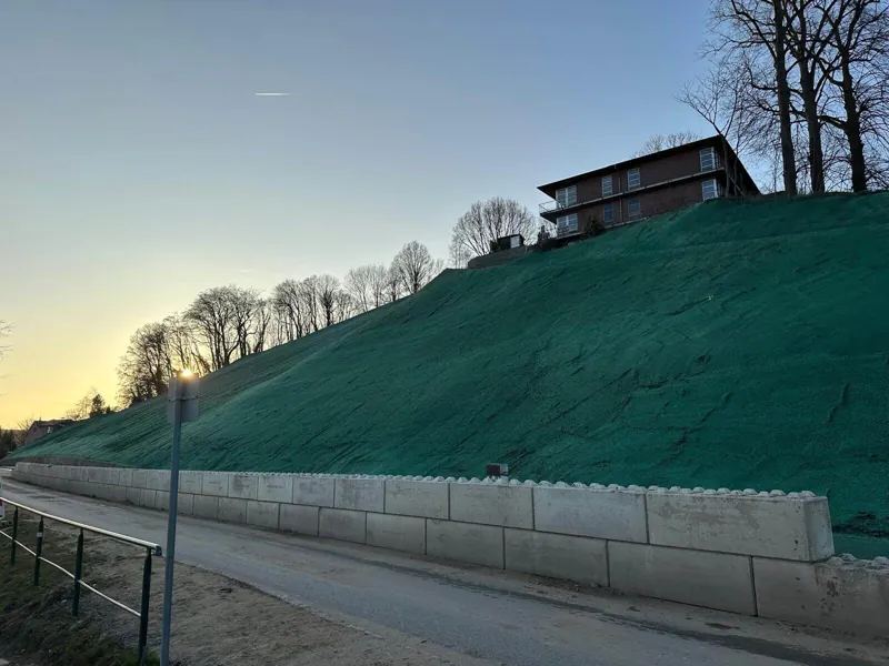 Lange Böschung mit grüner Nassansaat-Schicht über einer Stützmauer, im Abendlicht