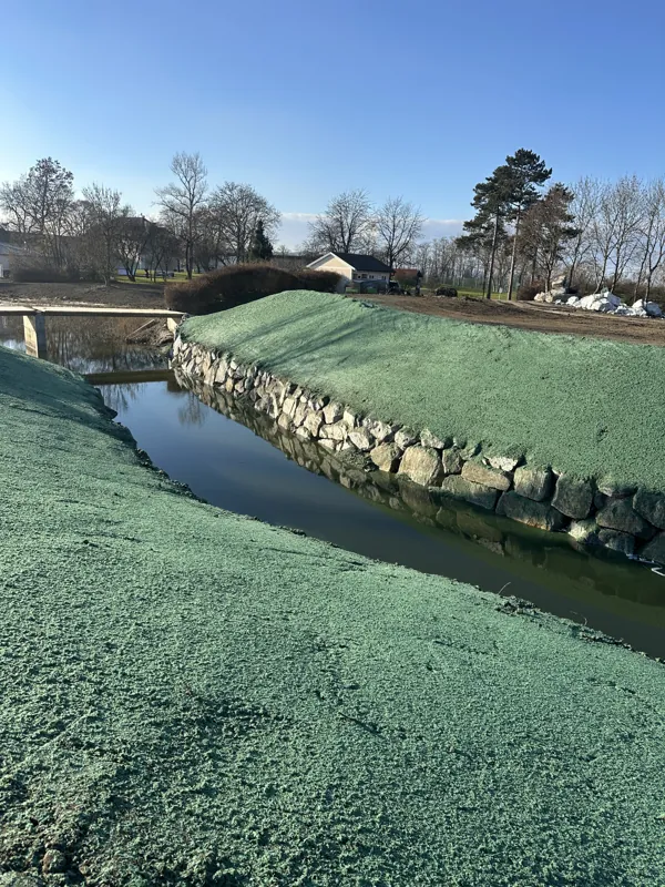 Beide Uferböschungen eines Bachs mit Wasserbausteinen, oberhalb grün angespritzt