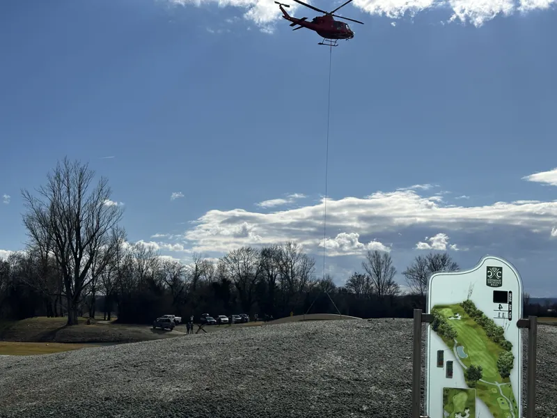 Hubschrauber mit Außenlastbehälter über einer frisch modellierten Fläche auf einem Golfplatz