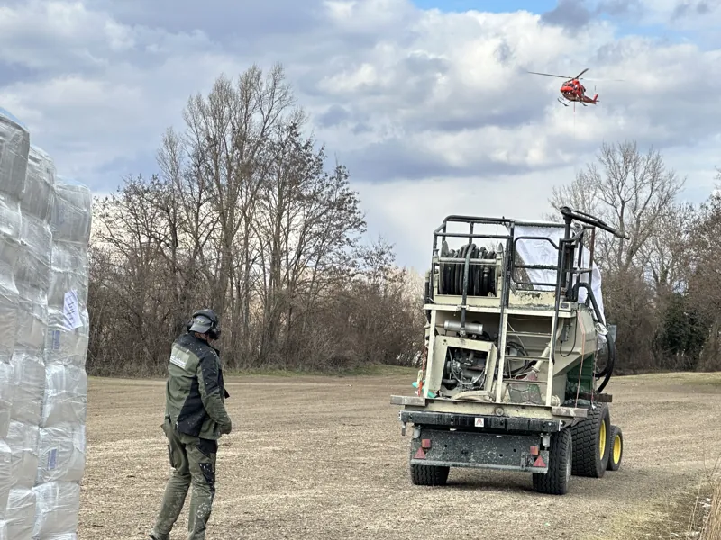 Mitarbeiter neben einem geländegängigen Hydroseeder, im Hintergrund ein Hubschrauber